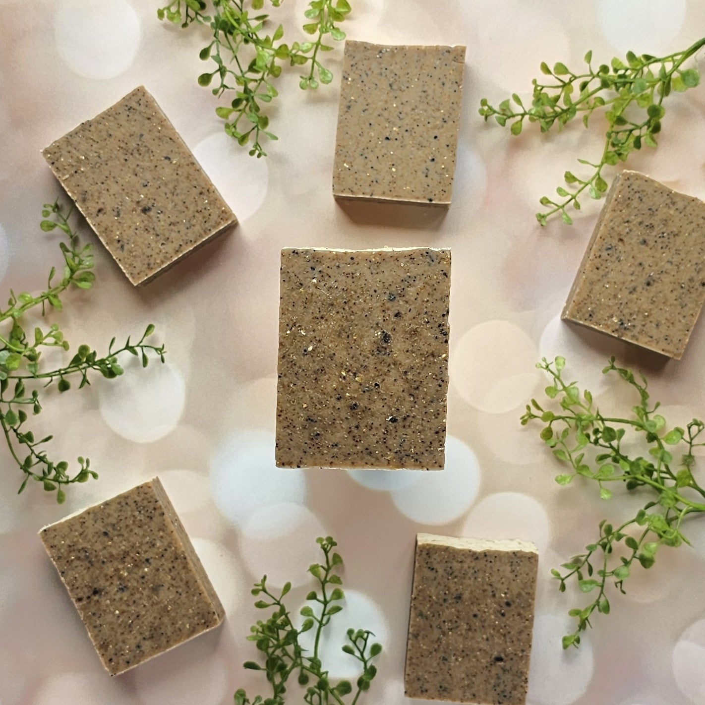 Six rectangular Gardener Goat Milk Soap bars by Amillia Acres, speckled and brown, are arranged in a circle on a light background with small green faux leaves.