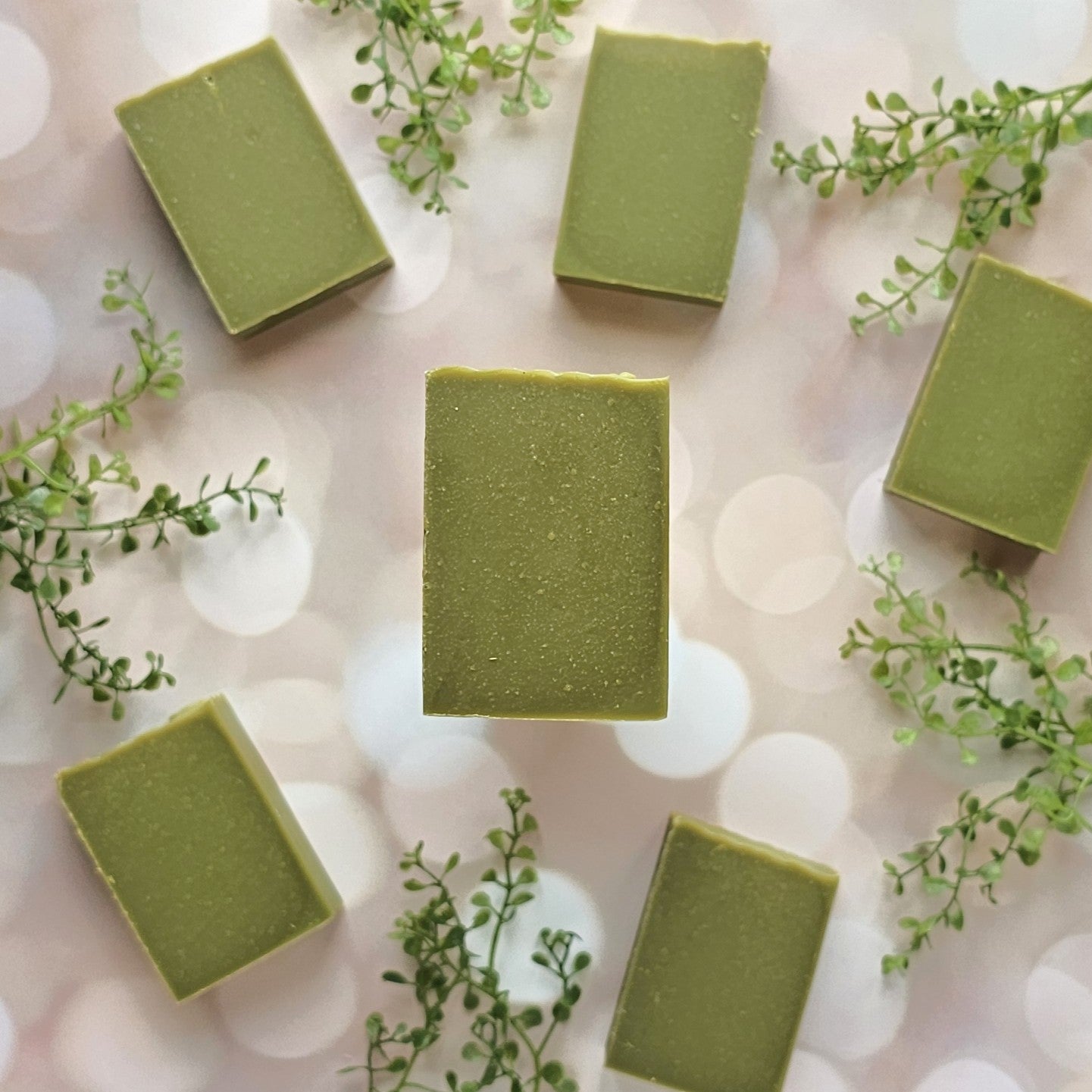 Six Minty (Essential Oil) Goat Milk Soap bars from Amillia Acres ~ Goat Milk Soaps and Lotions are arranged on a soft, blurred background, with small green leaf sprigs between them for a fresh, natural look.