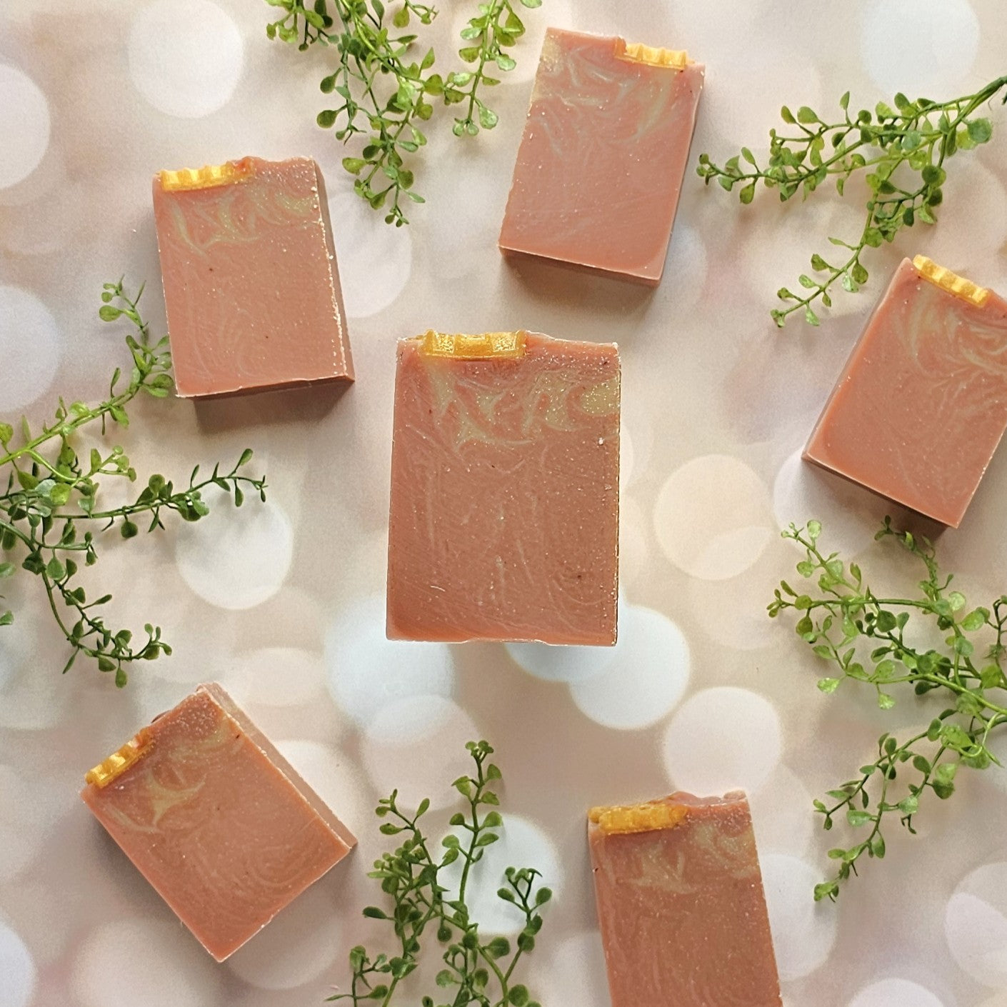 Six Amillia Acres Rose Clay & Honey Goat Milk Soap bars with marbled patterns are arranged on a light, bokeh-patterned surface, accented by green sprigs.