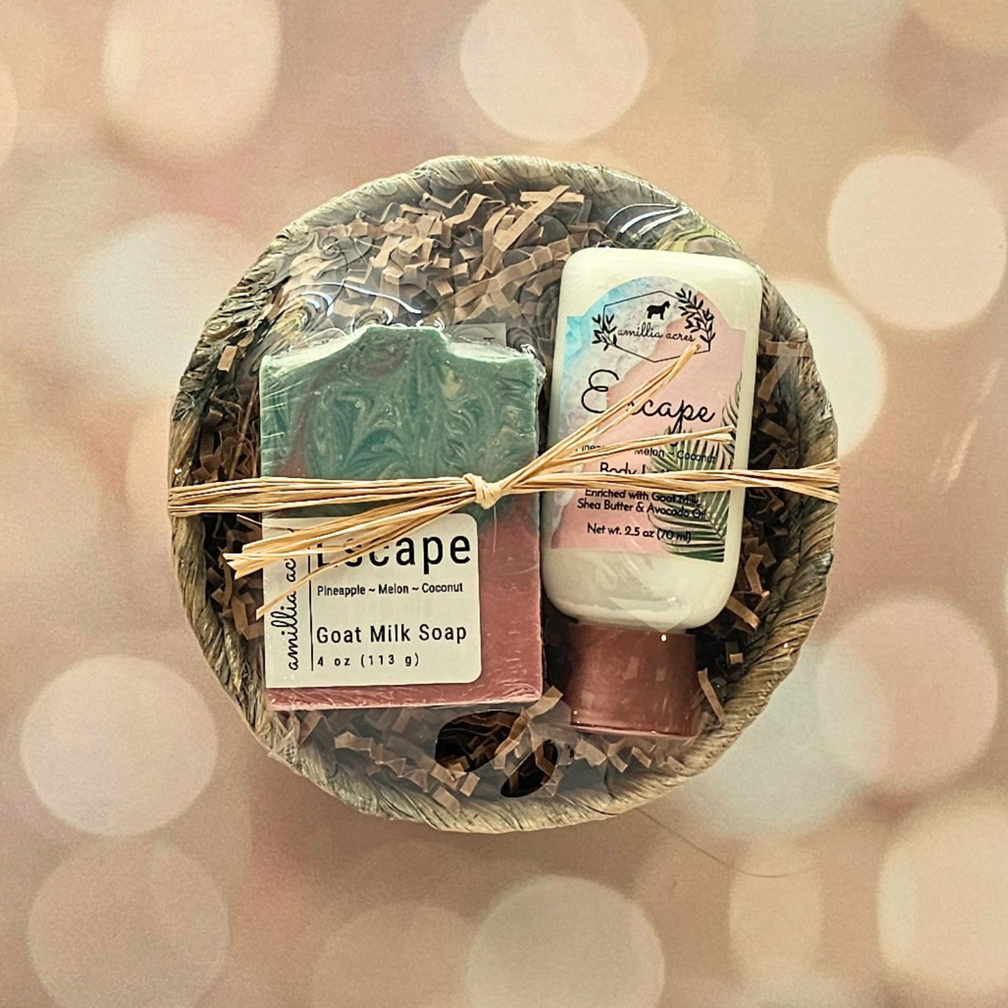 The Small Gift Basket by Amillia Acres ~ Goat Milk Soaps and Lotions features shredded paper, a goat milk bar soap, triple butter lip balm, and "Escape" lotion, all tied with raffia against a softly blurred background with gentle light spots.