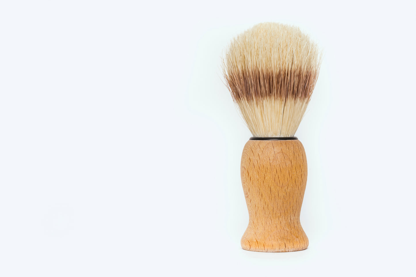 The Amillia Acres Classic Shave Brush features a wooden handle and light and dark bristles, standing upright on a simple background—an essential addition to any refined shaving routine.