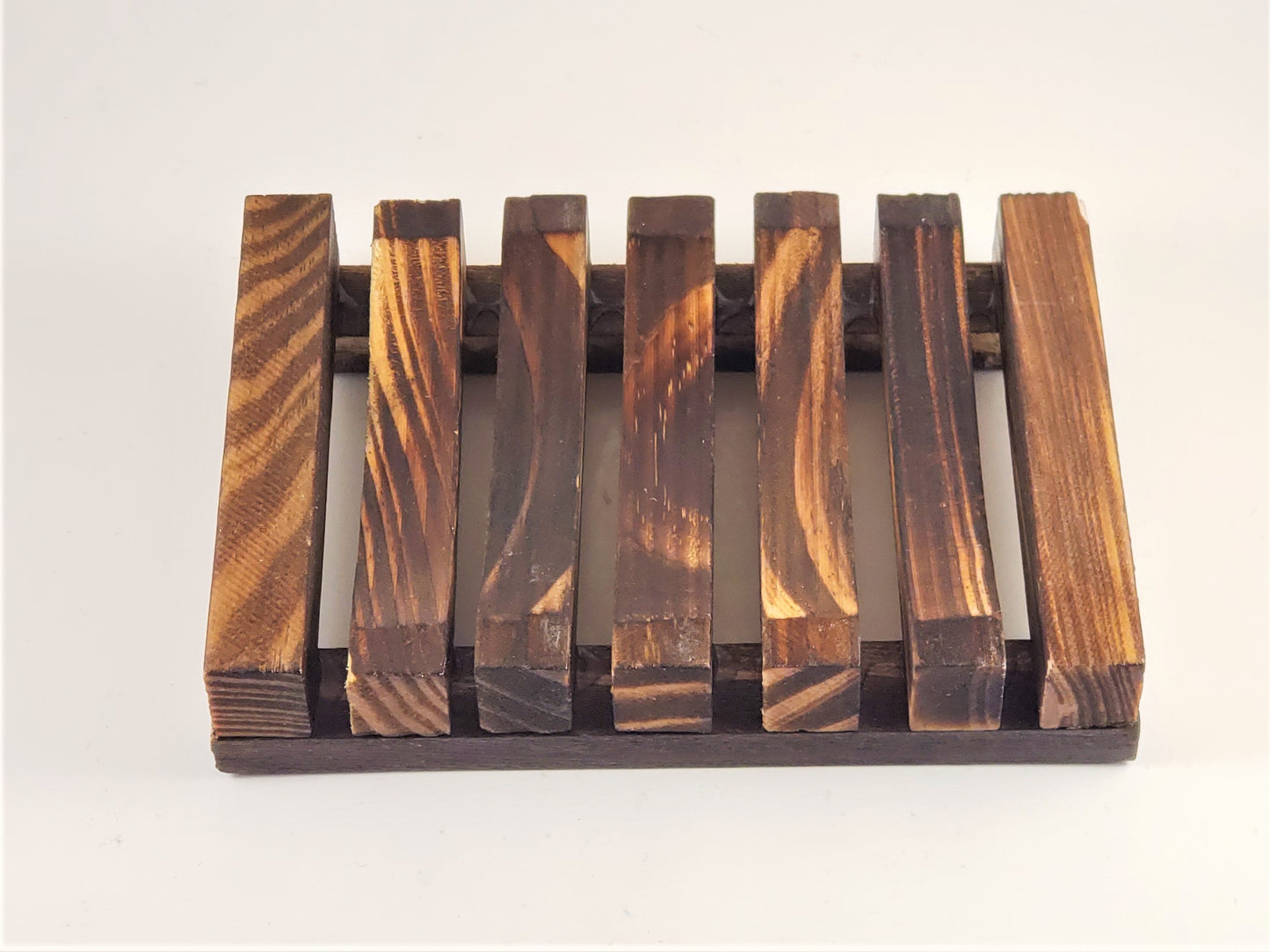 Introducing the Amillia Acres Wooden Soap Lift: a compact soap saver featuring dark brown wooden slats arranged in parallel fashion, highlighting their natural wood grain patterns. These slightly elevated slats form a grid-like design, providing an effective and all-natural solution for keeping your soap dry.
