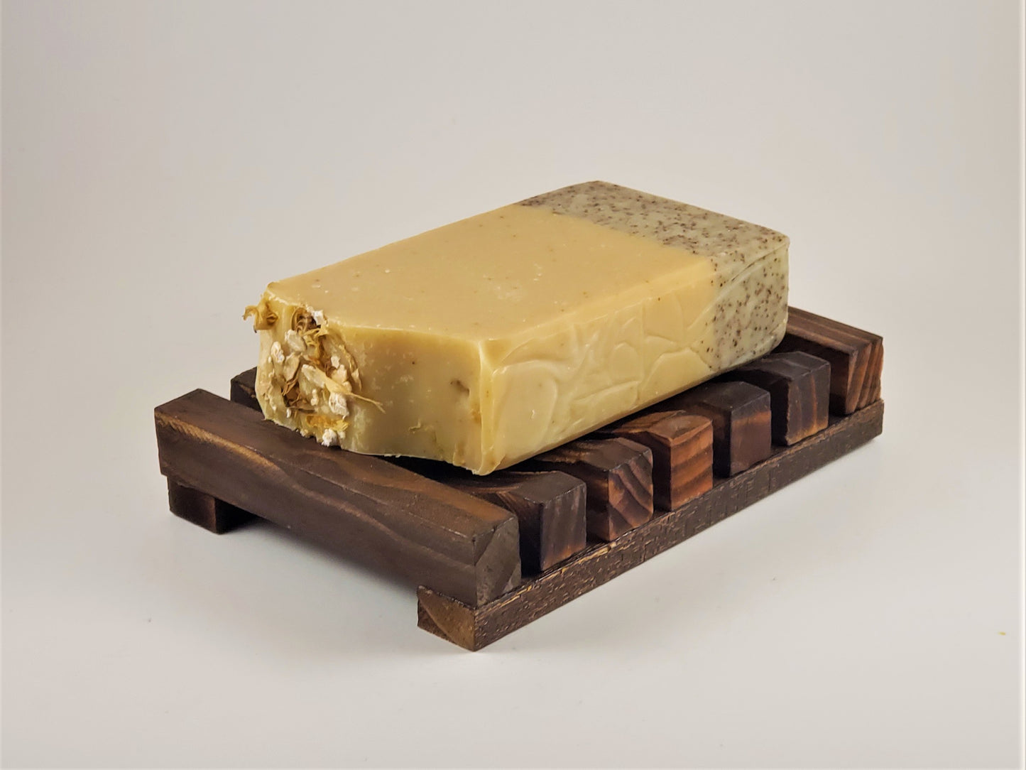 A two-toned, oatmeal-infused natural soap bar with a textured top is showcased on an Amillia Acres Wooden Soap Lift set against a white background, ensuring the soap remains dry and lasts longer.