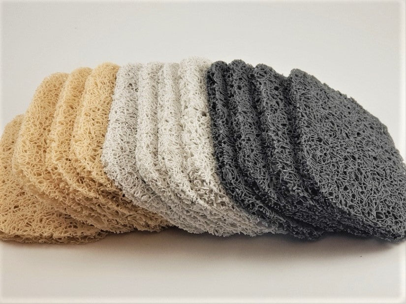 A collection of Amillia Acres Soap Saver pads is displayed in four elegant color variations: beige, light gray, white, and dark gray. Each stack features multiple pads arranged in an overlapping manner against a neutral backdrop. These soap savers are crafted to enhance the longevity of your soap while adding a touch of style and functionality.