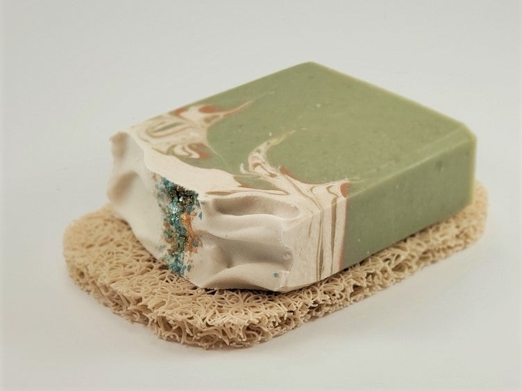 A handcrafted bar of soap with a green and white marbled design, featuring hints of blue, rests gracefully on the beige-textured Amillia Acres' Soap Saver to help maximize the lifespan of your soap.