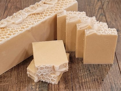 Nourish | Goat Milk Soap by Amillia Acres is showcased on a wooden surface. A large bar with a honeycomb pattern is cut into smaller rectangular bars of beige, handmade soap infused with natural oils and neatly stacked or laid flat.