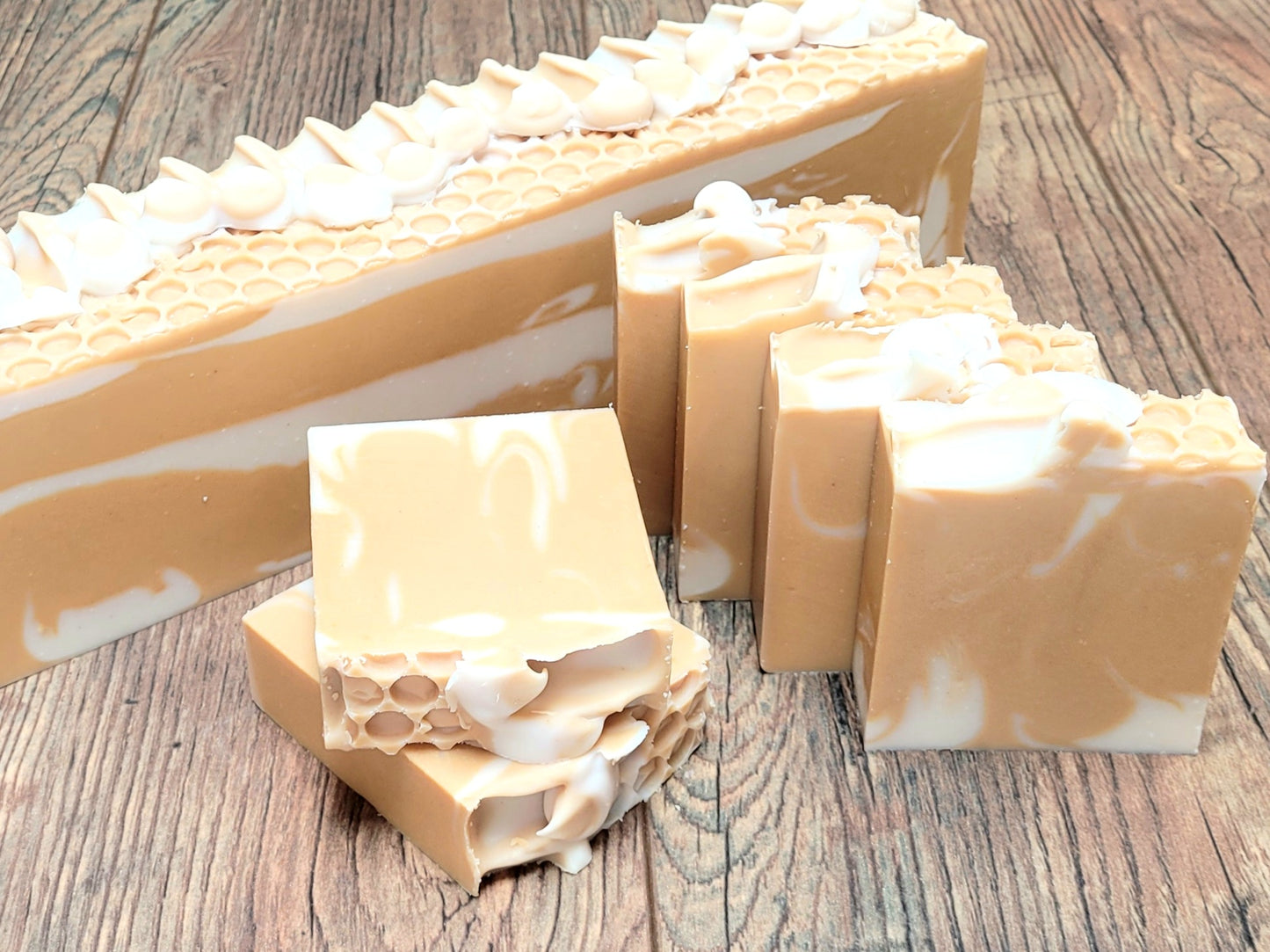 Amillia Acres' Nourish Goat Milk Soap, infused with natural oils, features a honeycomb texture and swirling beige and white patterns. Elegantly cut bars rest on a wooden surface in front of a larger loaf, showcasing the artisanal charm of this handcrafted soap.