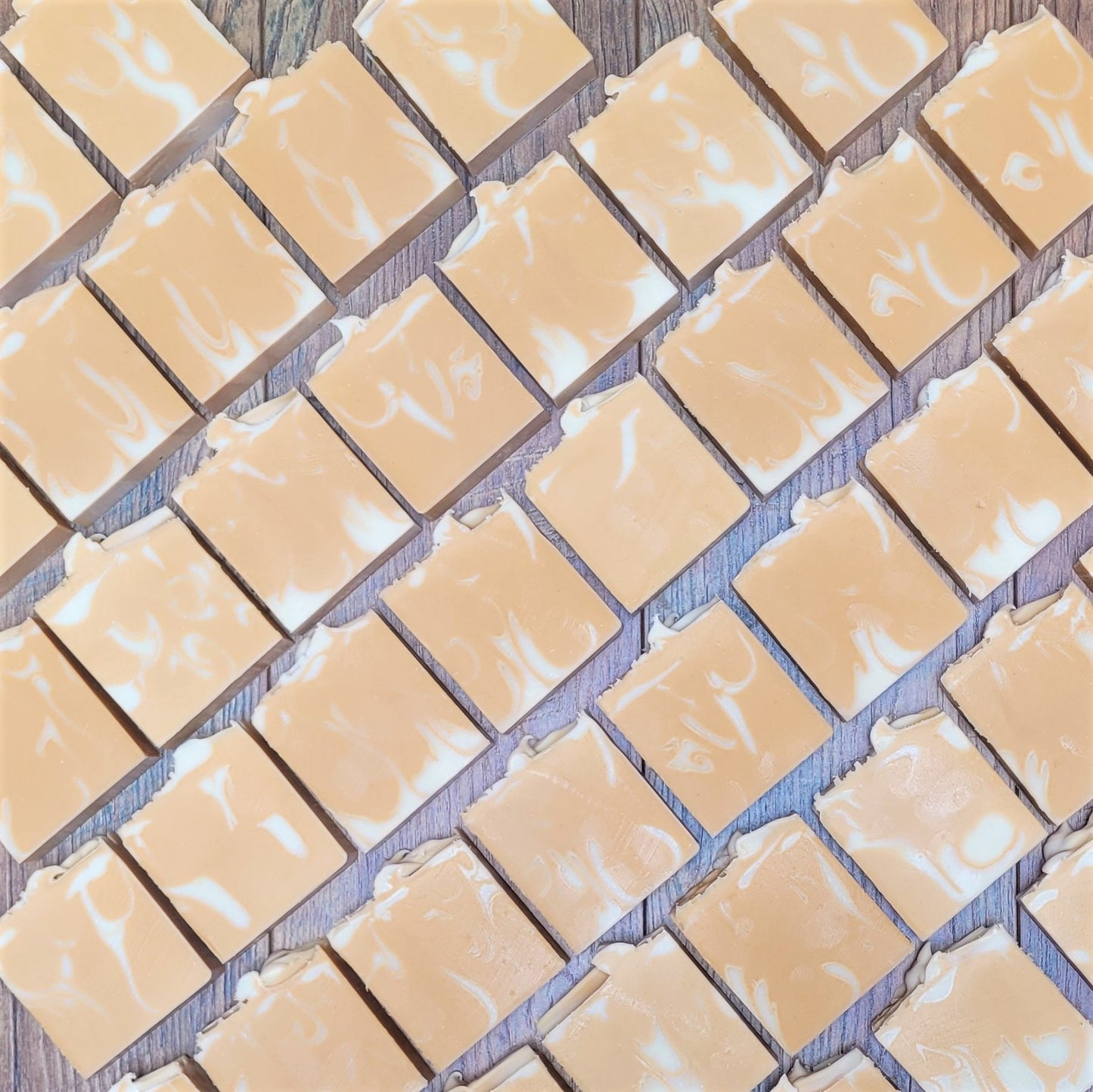 Diagonal handmade Nourish goat milk soap bars by Amillia Acres, featuring white swirls, are displayed on a wooden surface, highlighting their natural oils.