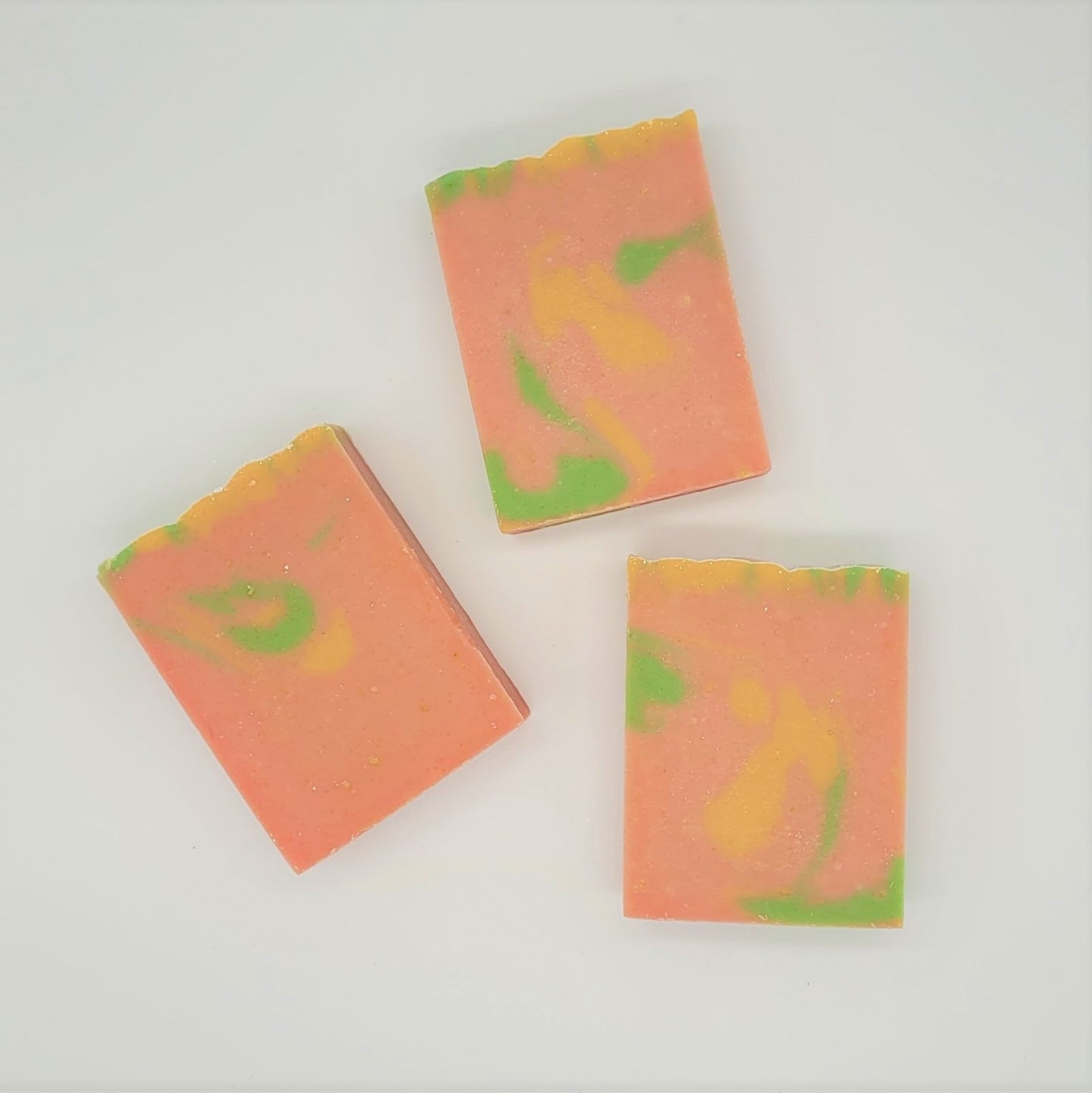 Three bars of Amillia Acres' "Happiness" goat milk soap, featuring a marbled pink, yellow, and green design, are arranged on a light background.