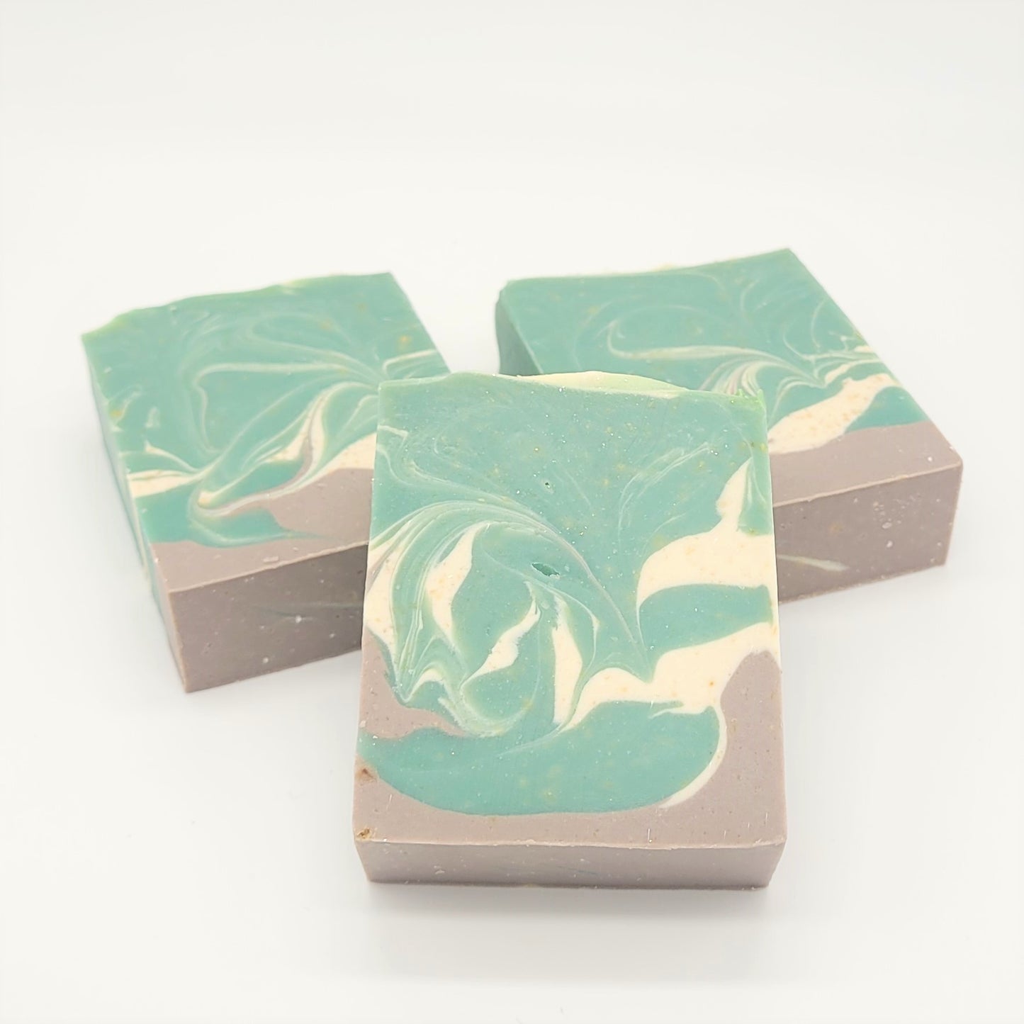 Three rectangular bars of Amillia Acres' Relax Goat Milk Soap feature a marbled teal, cream, and light brown design. Crafted with natural oils, they are displayed on a plain white background.