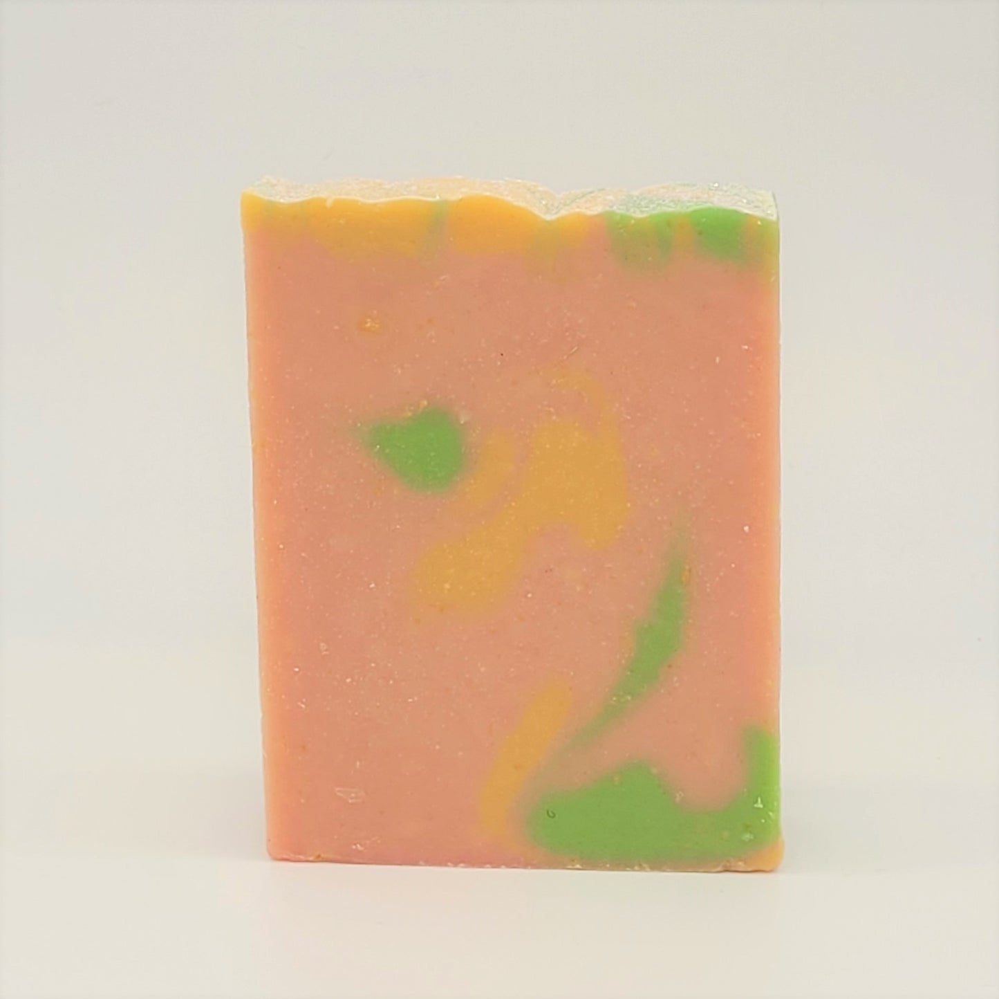 The Happiness Goat Milk Soap from Amillia Acres stands upright, showcasing a marbled design of pink with green and yellow swirls. Crafted with nourishing natural oils, this handmade soap promises an indulgent experience.