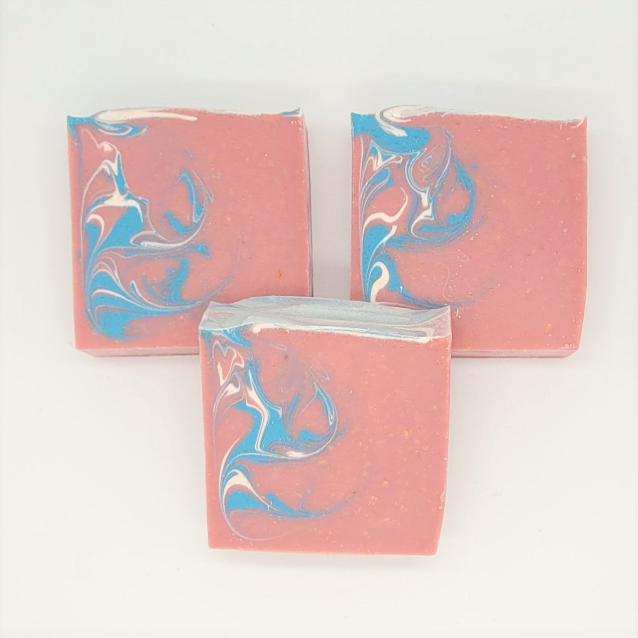 A trio of Escape goat milk soaps by Amillia Acres, with pink bases and marbled blue-white swirls, invite an escape into fragrance on a white background.