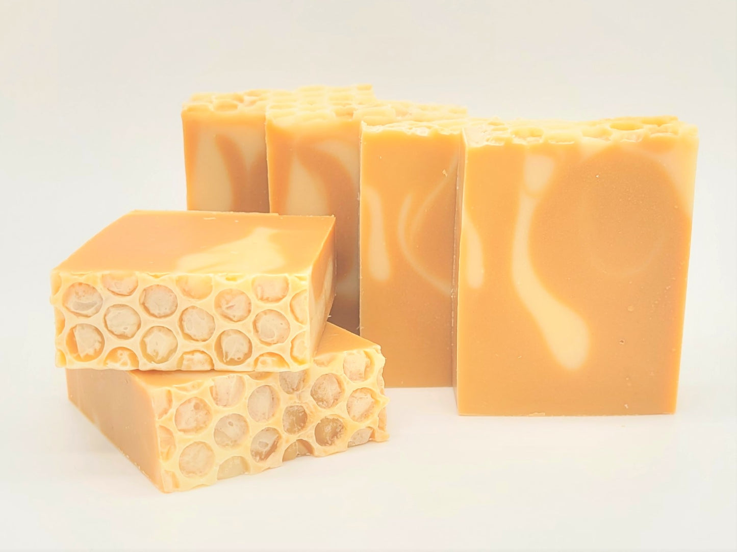 Five Amillia Acres Nourish Goat Milk Soap bars sit against a light backdrop. Two display the honeycomb top, and others show smooth swirled sides. Made with natural oils, the soap features a warm honey-like hue.