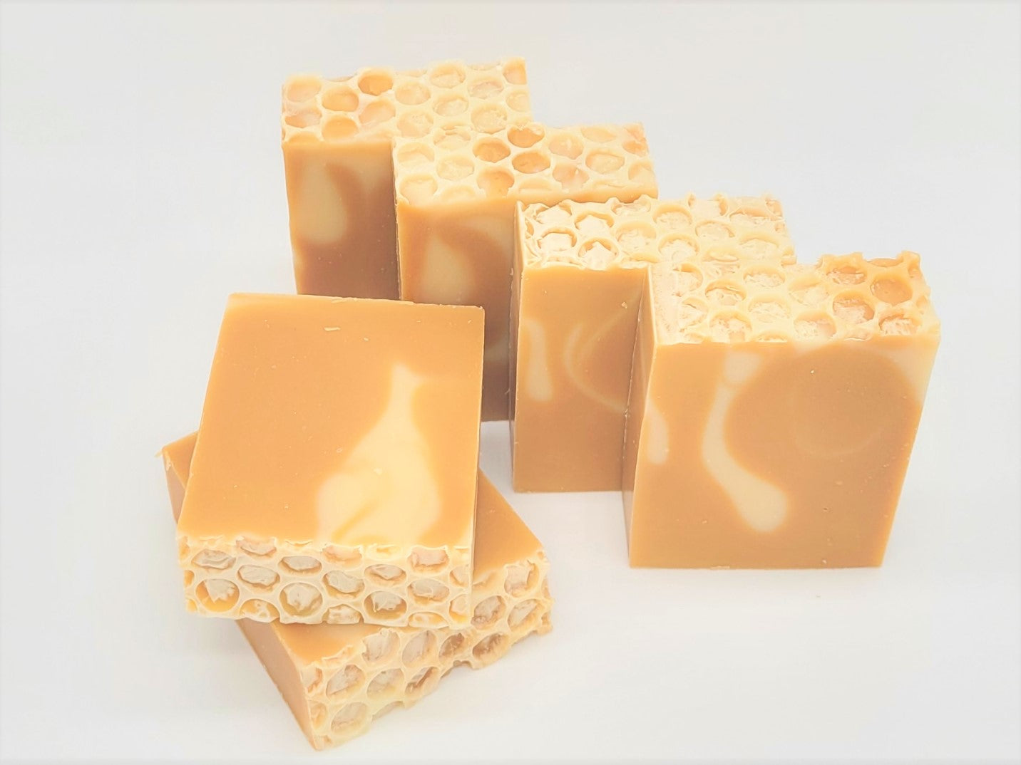 Bars of Amillia Acres' Nourish Goat Milk Soap, displaying honeycomb patterns in light brown and cream, are arranged on a white surface. Crafted with natural oils, the soap features a blend of smooth and textured sections resembling honeycomb tops.