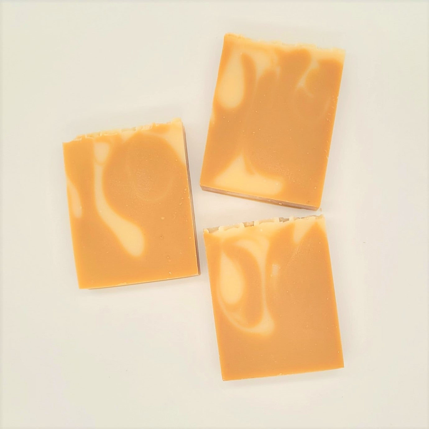 Three rectangular bars of Amillia Acres' Nourish Goat Milk Soap, infused with natural oils, showcase a marbled orange and creamy white pattern while resting on a plain white background.