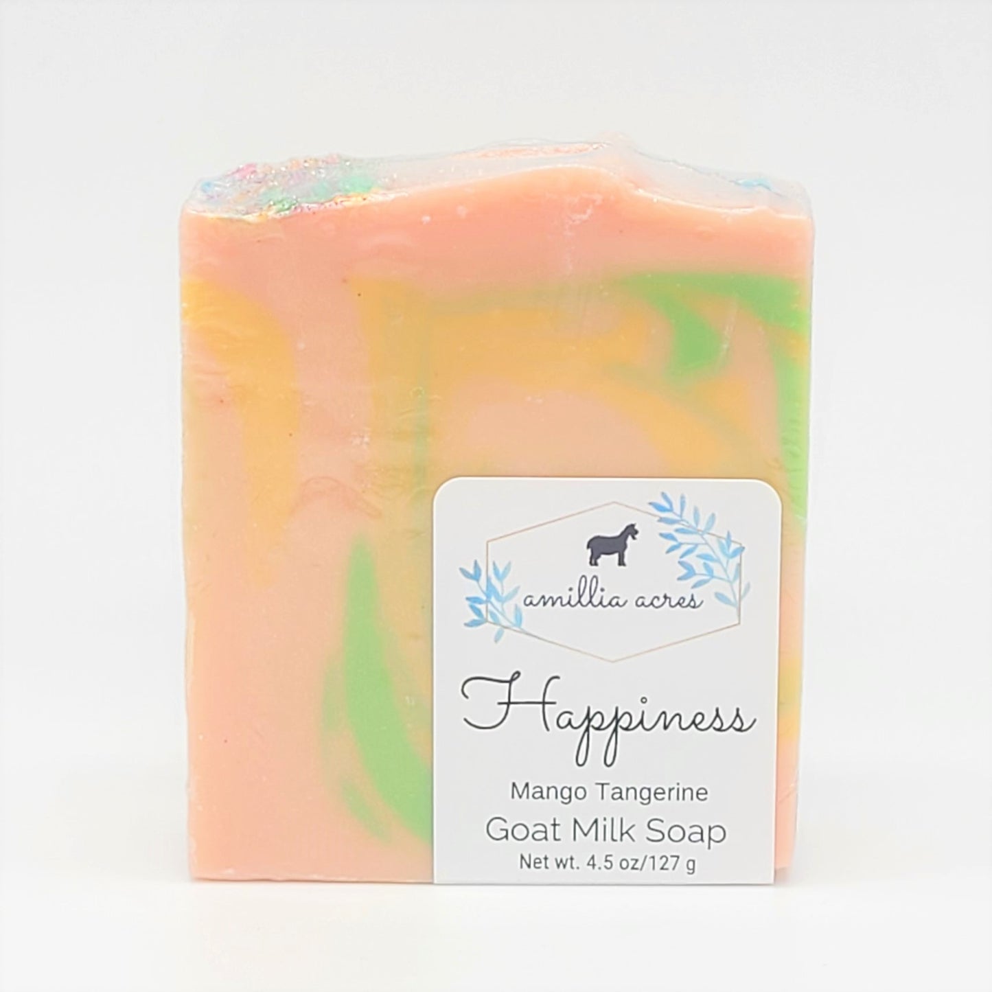 A 4.5 oz/127 g goat milk soap bar swirled with peach, green, and yellow colors features the label "Amillia Acres ~ Goat Milk Soaps and Lotions, Happiness, Mango Tangerine." Made with natural oils, this luxurious handmade soap showcases artisanal craftsmanship.