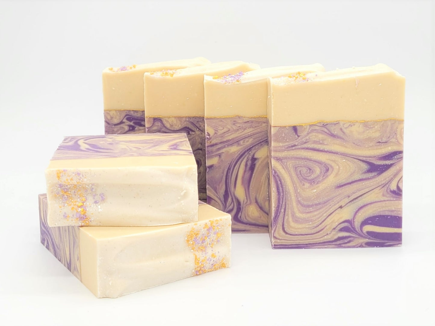Five bars of Amillia Acres' Grace | Goat Milk Soap, adorned with purple and cream swirls, feature glitter specks and an elegant design. Some bars lie flat while others are upright, all set against a plain white background.