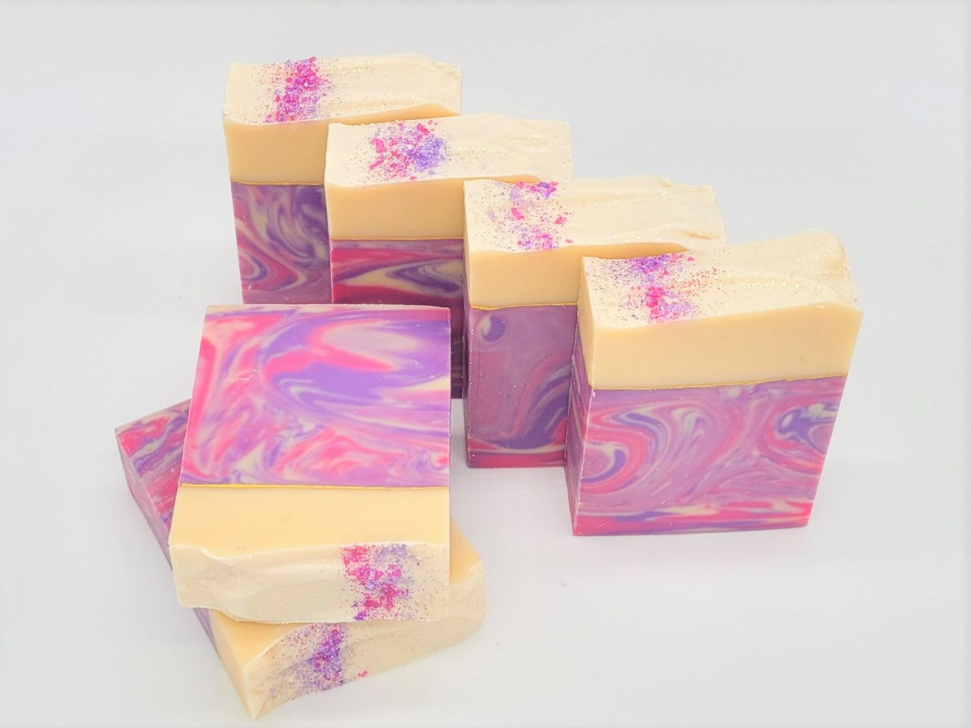 Five Dazzle Goat Milk Soaps from Amillia Acres are stacked upright, featuring swirling pink, purple, and cream patterns with pink and purple speckles on top. Made with natural oils, they rest on a plain white surface.