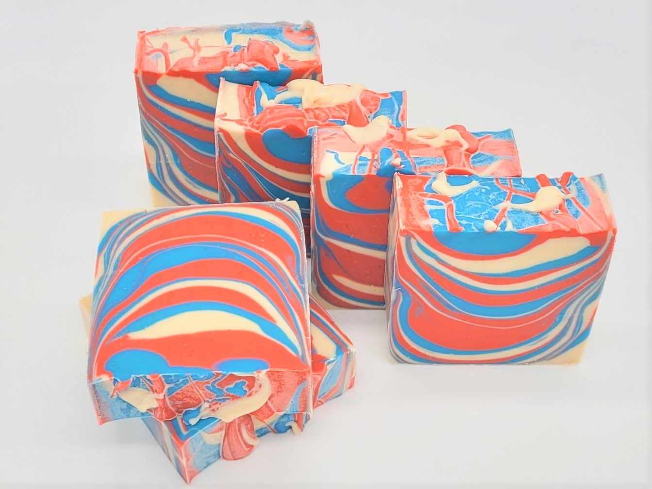 Six handmade bars of Amillia Acres' "Barbershop" goat milk soap are stacked on a light surface, displaying vibrant swirls of red, blue, and cream. Each bar features playful abstract patterns that embody artisanal charm.