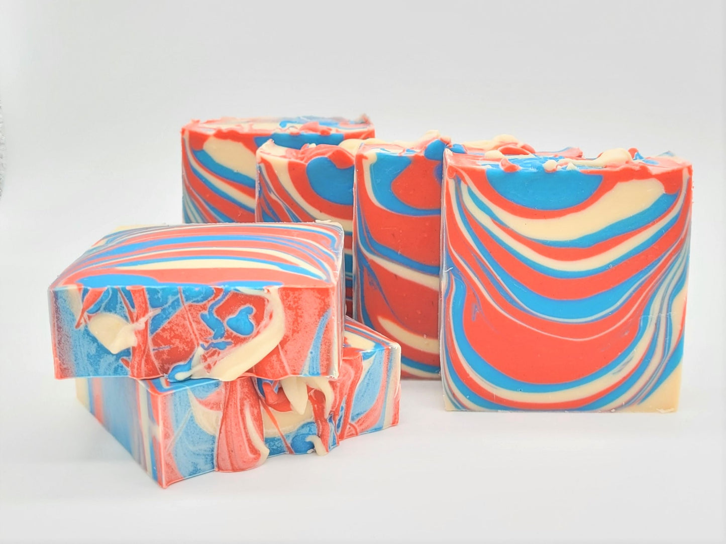 A set of four Barbershop Goat Milk Soaps from Amillia Acres, featuring vibrant red, blue, and cream swirls on a white background, showcase a visually striking marble-like design reminiscent of barbershop soap artistry.