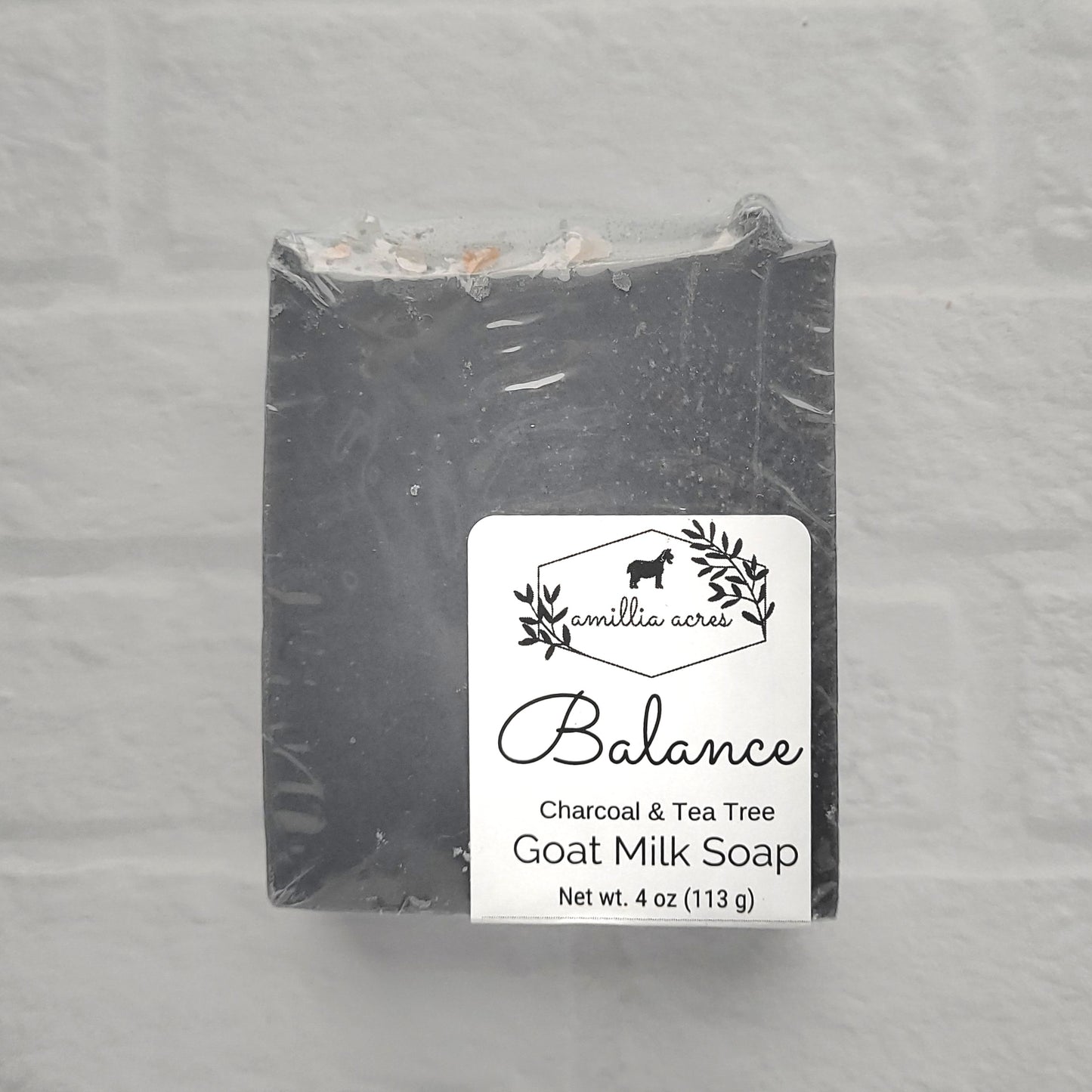 The 4 oz "Balance" goat milk soap from Amillia Acres includes activated charcoal and tea tree for a refreshing cleanse. Wrapped in plastic, it features the brand alongside a goat image.