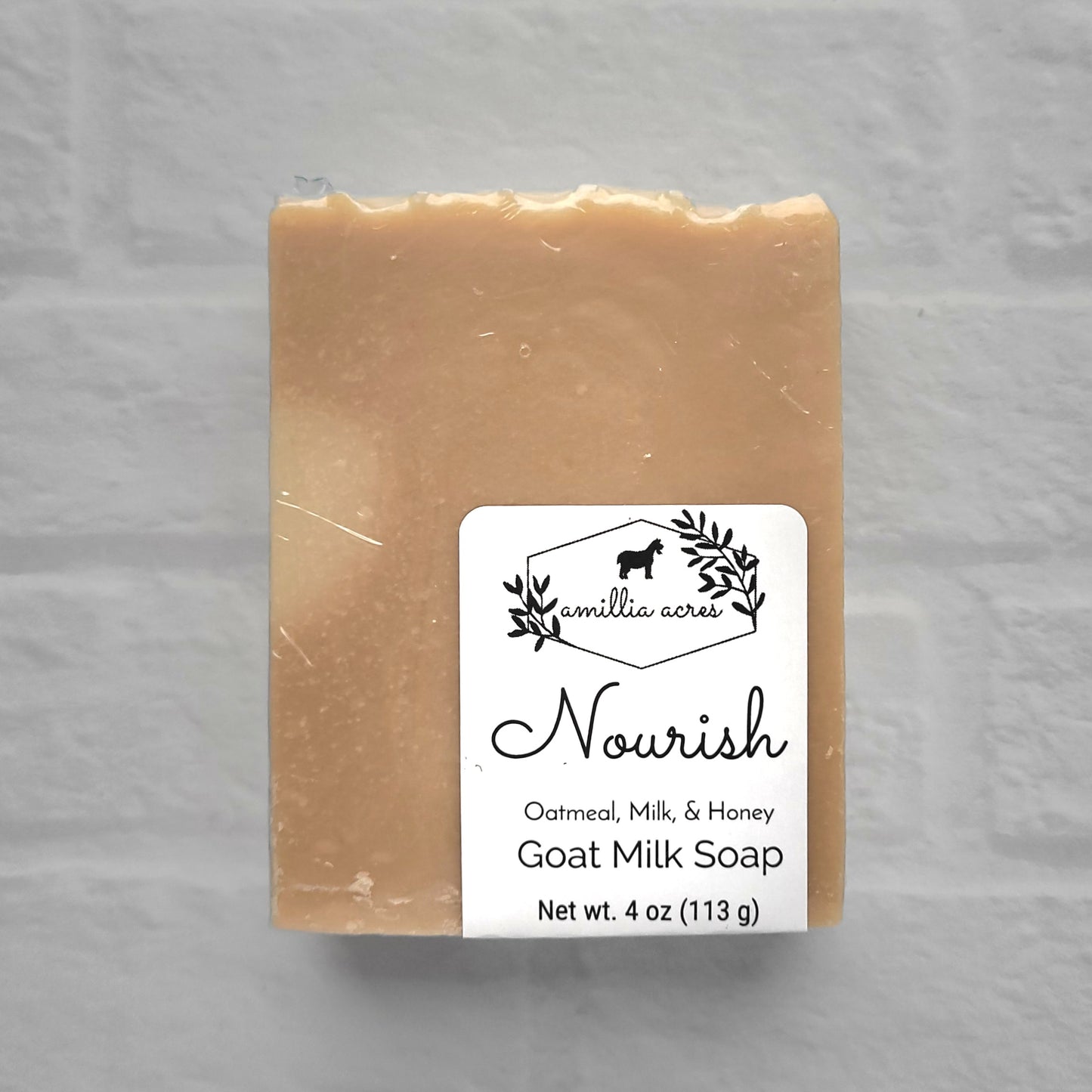 A 4 oz (113 g) bar of handmade goat milk soap, labeled "Nourish" by Amillia Acres, infused with oatmeal, milk, and honey. It rests against a white textured backdrop with the Amillia Acres logo on the label.
