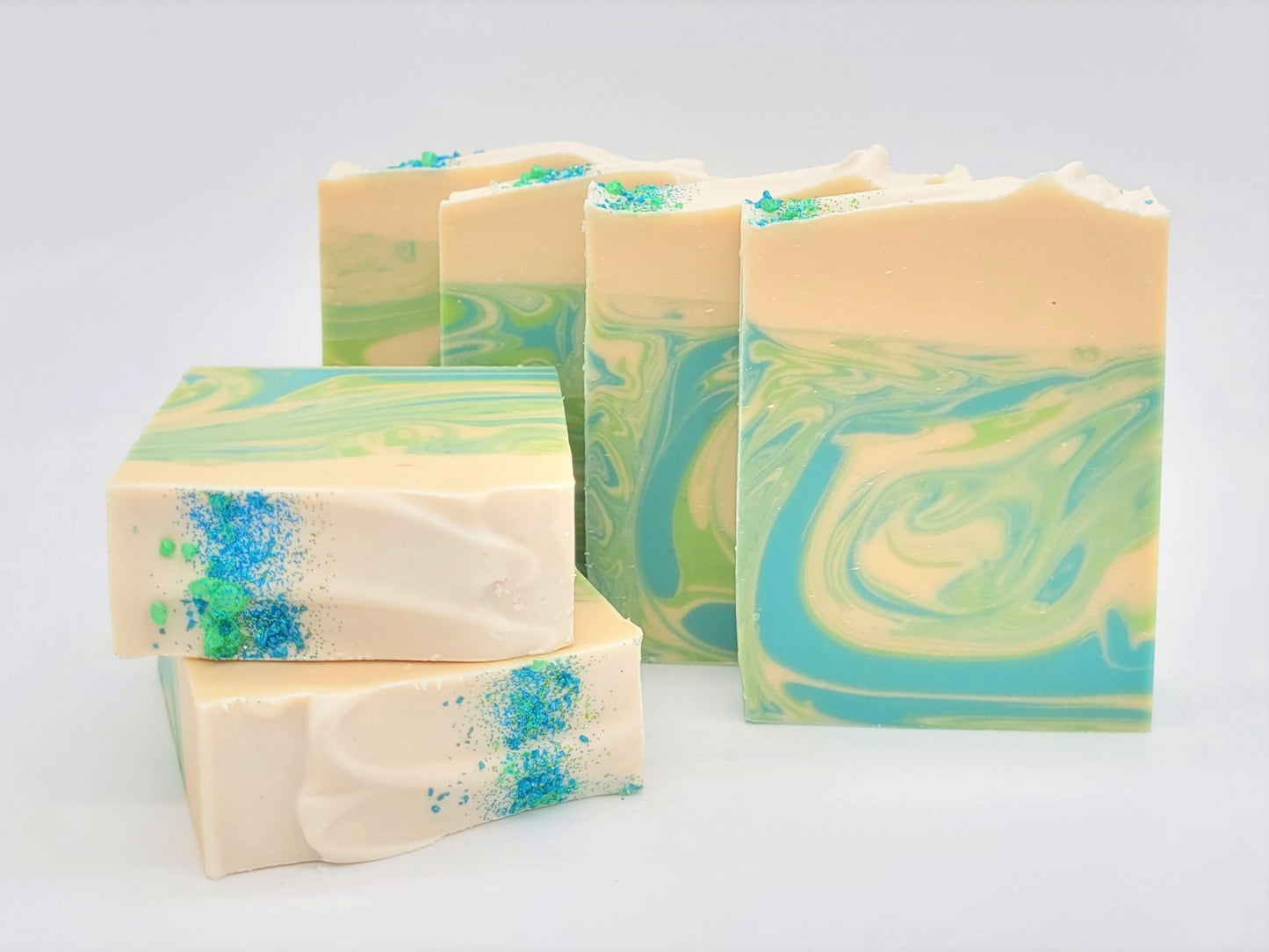 Amillia Acres' Awaken Goat Milk Soap, infused with eucalyptus and spearmint, stands upright against a light background. The handcrafted soap features marbled swirls of green, blue, and cream with specks of blue and green powder on two stacked bars.