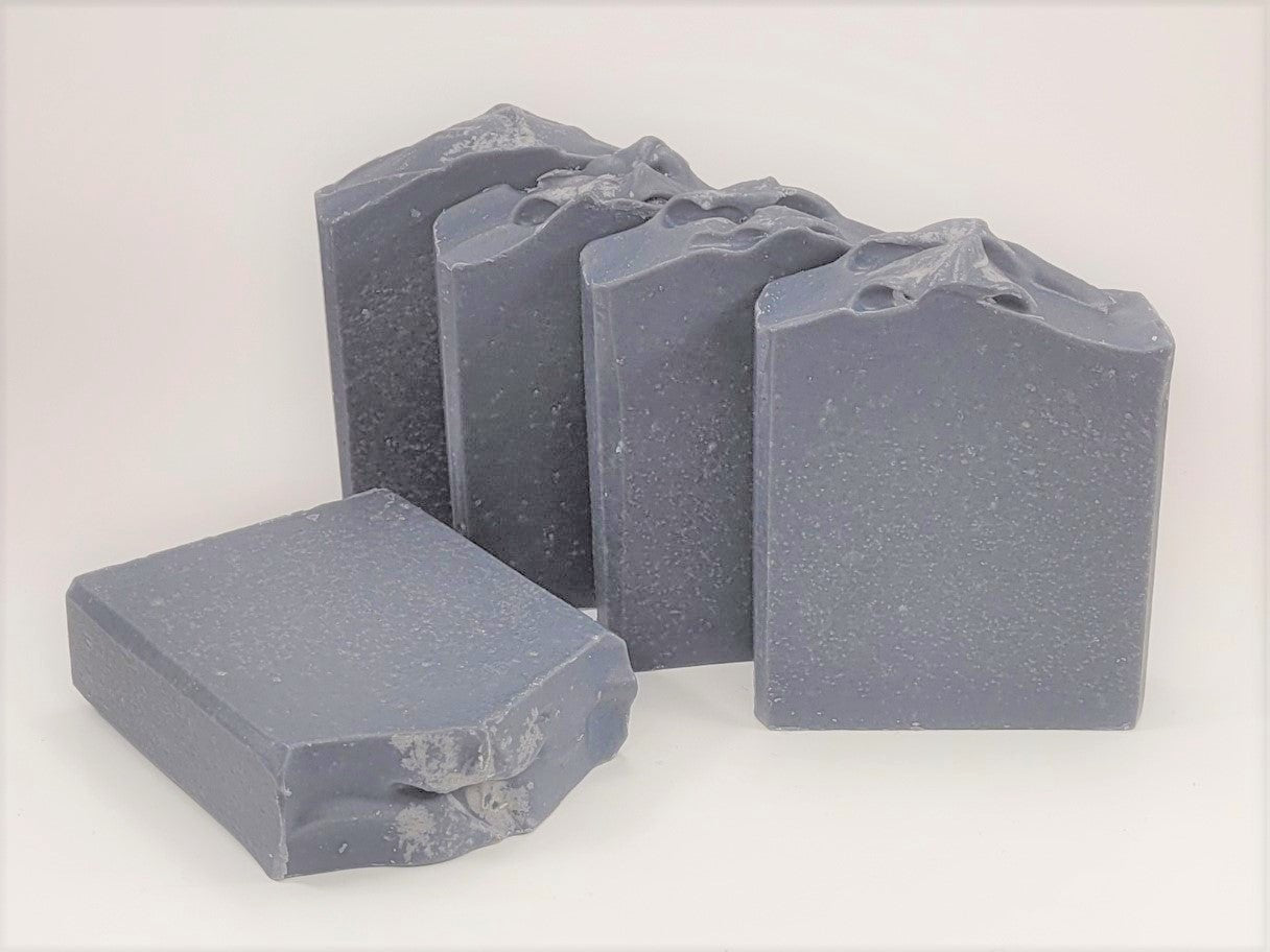 Five Balance goat milk soap bars from Amillia Acres, featuring textured tops and infused with tea tree essence, are arranged on a light surface. One bar lies flat in the foreground while the other four stand upright, slightly overlapping each other.