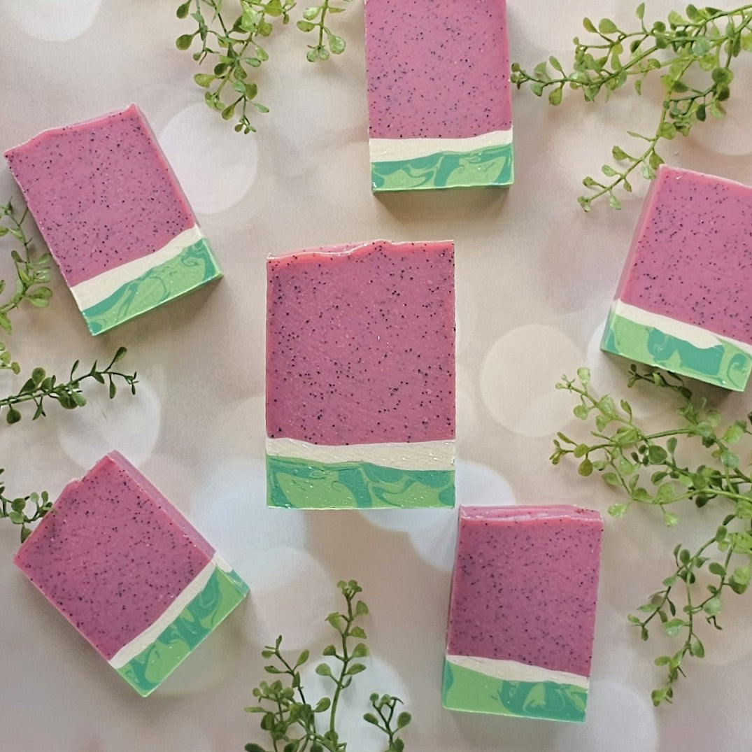 Five Melon Baby goat milk soap bars by Amillia Acres ~ Goat Milk Soaps and Lotions, featuring pink, white, and green layers, are displayed with green sprigs for a fresh, summery watermelon-inspired look.