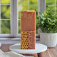 Three rectangular bars of Amillia Acres Rose Clay & Honey Goat Milk Soap are stacked on a white stand. The lower bars show honeycomb patterns and are displayed by a window next to a potted green plant.