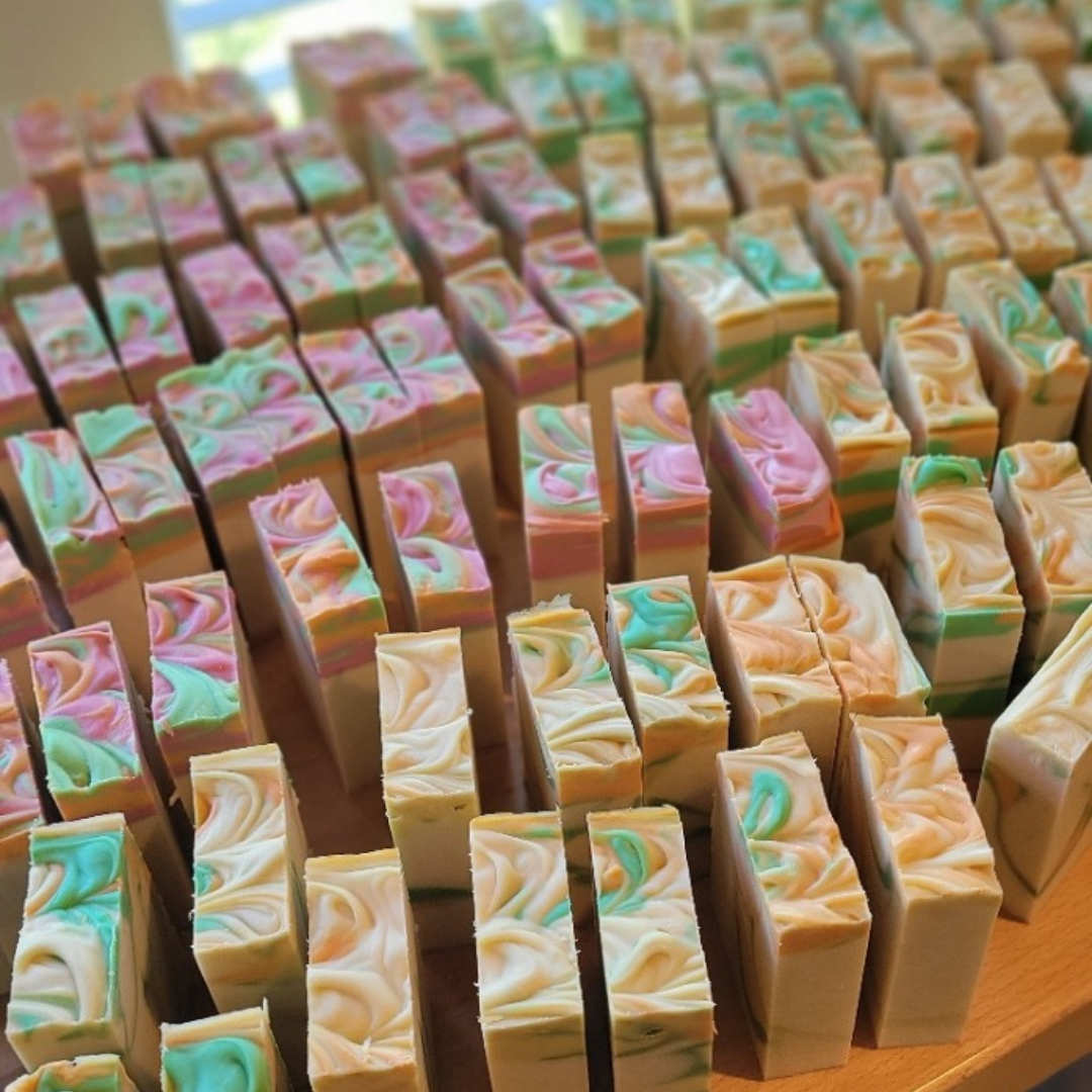 Displayed is the Mystery Soap Set (6 pack) by Amillia Acres ~ Goat Milk Soaps and Lotions, featuring handmade bars with swirled pastel patterns in pink, green, and blue hues. Each soap surprise is neatly arranged on a light wooden surface, offering a delightful aesthetic experience.