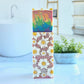 The Flower Child Goat Milk Soap by Amillia Acres showcases detailed daisies on a textured base, topped with a rainbow swirl, set against a backdrop of a white tub and potted plant in an airy room—highlighting the elegance of handcrafted soaps with natural oils.