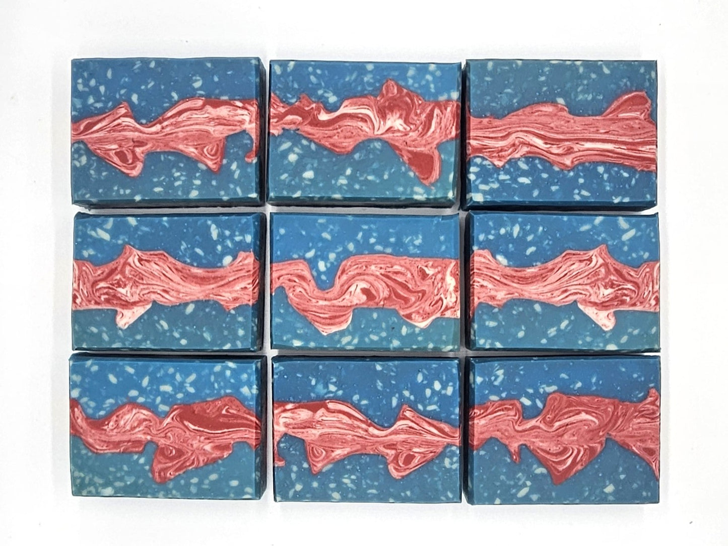 Nine Liberty Goat Milk Soap bars by Amillia Acres ~ Goat Milk Soaps and Lotions, each blue with white speckles and a wavy marbled red-and-white stripe, are arranged in a neat 3x3 grid on a white background.