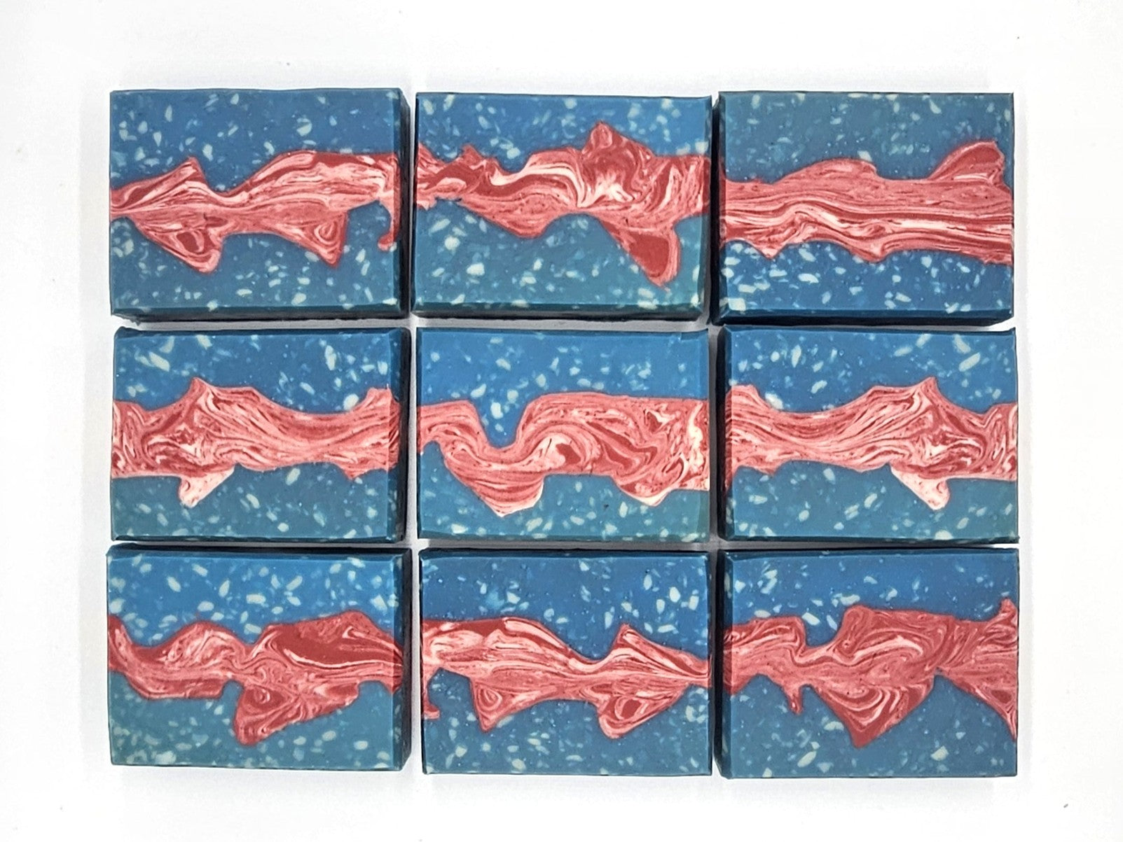 Nine Liberty Goat Milk Soap bars by Amillia Acres ~ Goat Milk Soaps and Lotions, each blue with white speckles and a wavy marbled red-and-white stripe, are arranged in a neat 3x3 grid on a white background.