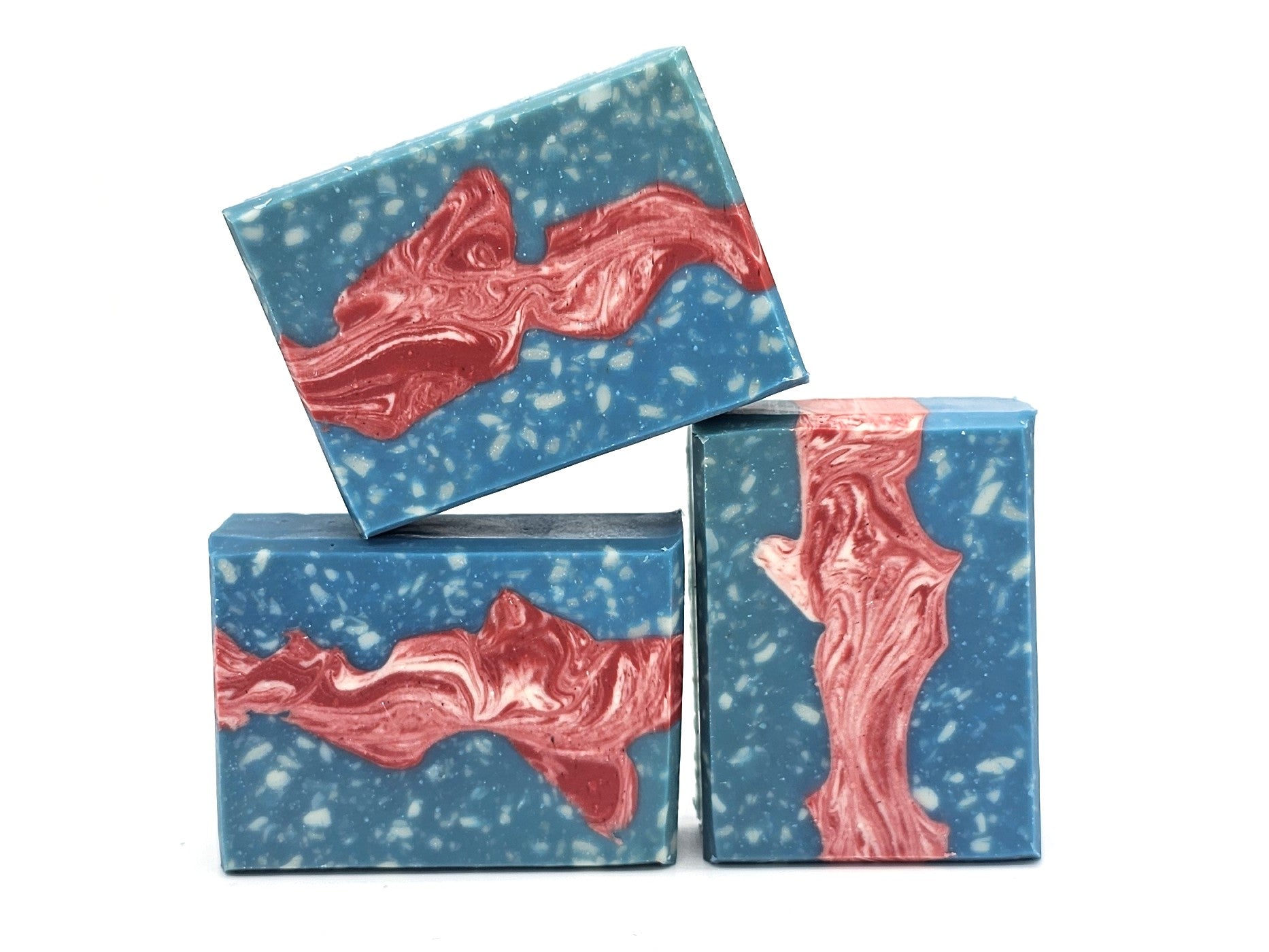 Three rectangular bars of Liberty Goat Milk Soap by Amillia Acres, featuring a blue base, white speckles, and a swirling red-pink marbled center, are stacked against a white background.