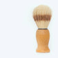 The Amillia Acres Classic Shave Brush features a wooden handle and light and dark bristles, standing upright on a simple background—an essential addition to any refined shaving routine.