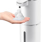 An individual holds their hand under an Amillia Acres ~ Goat Milk Soaps and Lotions Automatic Foaming Hand Soap Dispenser. The sleek, white design with silver accents dispenses foam soap touchlessly into the palm, while a semi-transparent window reveals its 4-level adjustable foam setting.