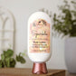 A bottle of Amillia Acres Sparkle Goat Milk Lotion sits on a wooden surface. The label reads "Cranberry & Sweet Orange" and features goat milk, shea butter, and avocado oil. A blurred plant appears in the background.