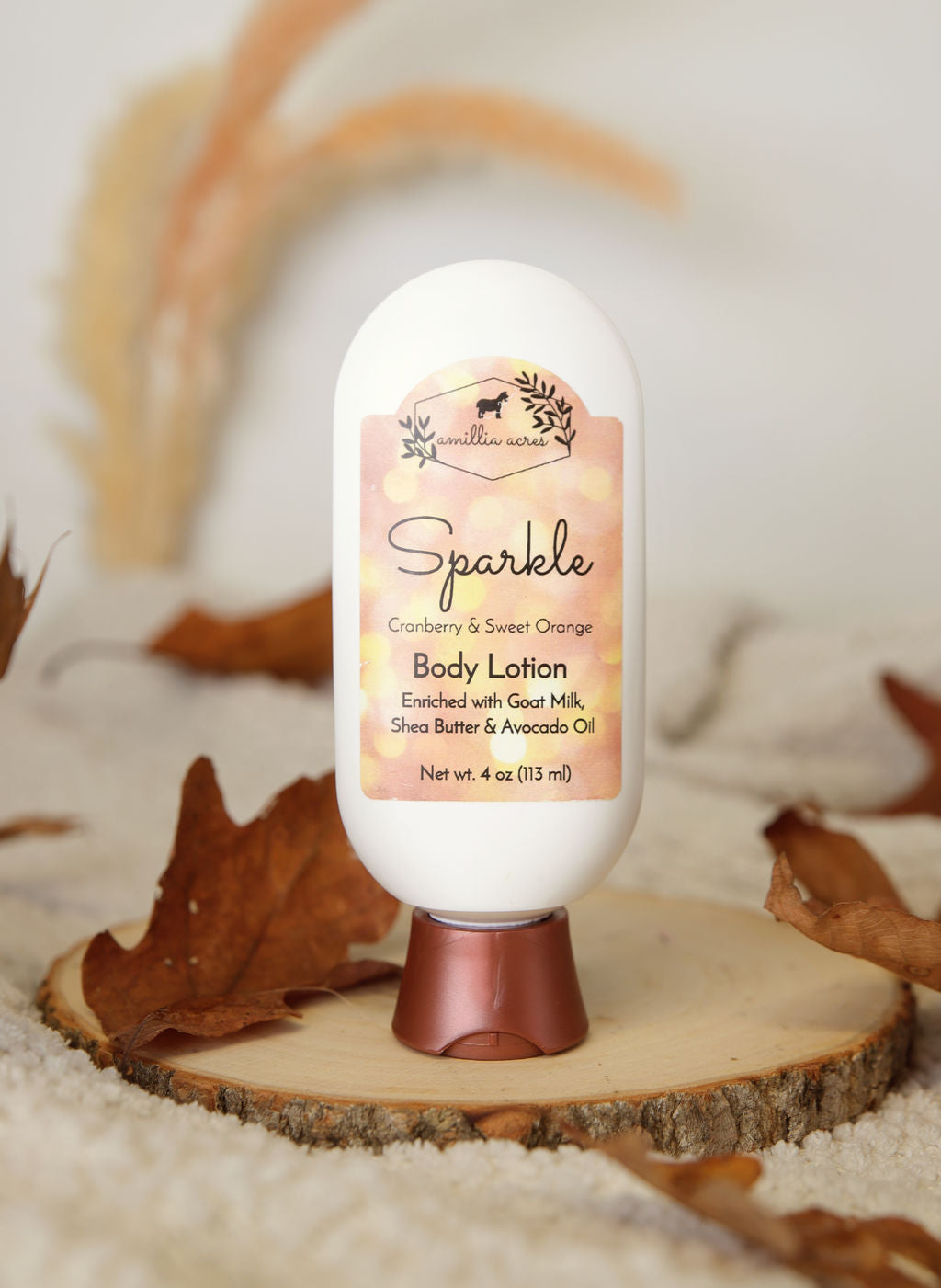 A bottle of Amillia Acres’ Sparkle Goat Milk Lotion rests on a wooden coaster with autumn leaves, featuring cranberry and sweet orange scent enriched with shea butter and avocado oil.