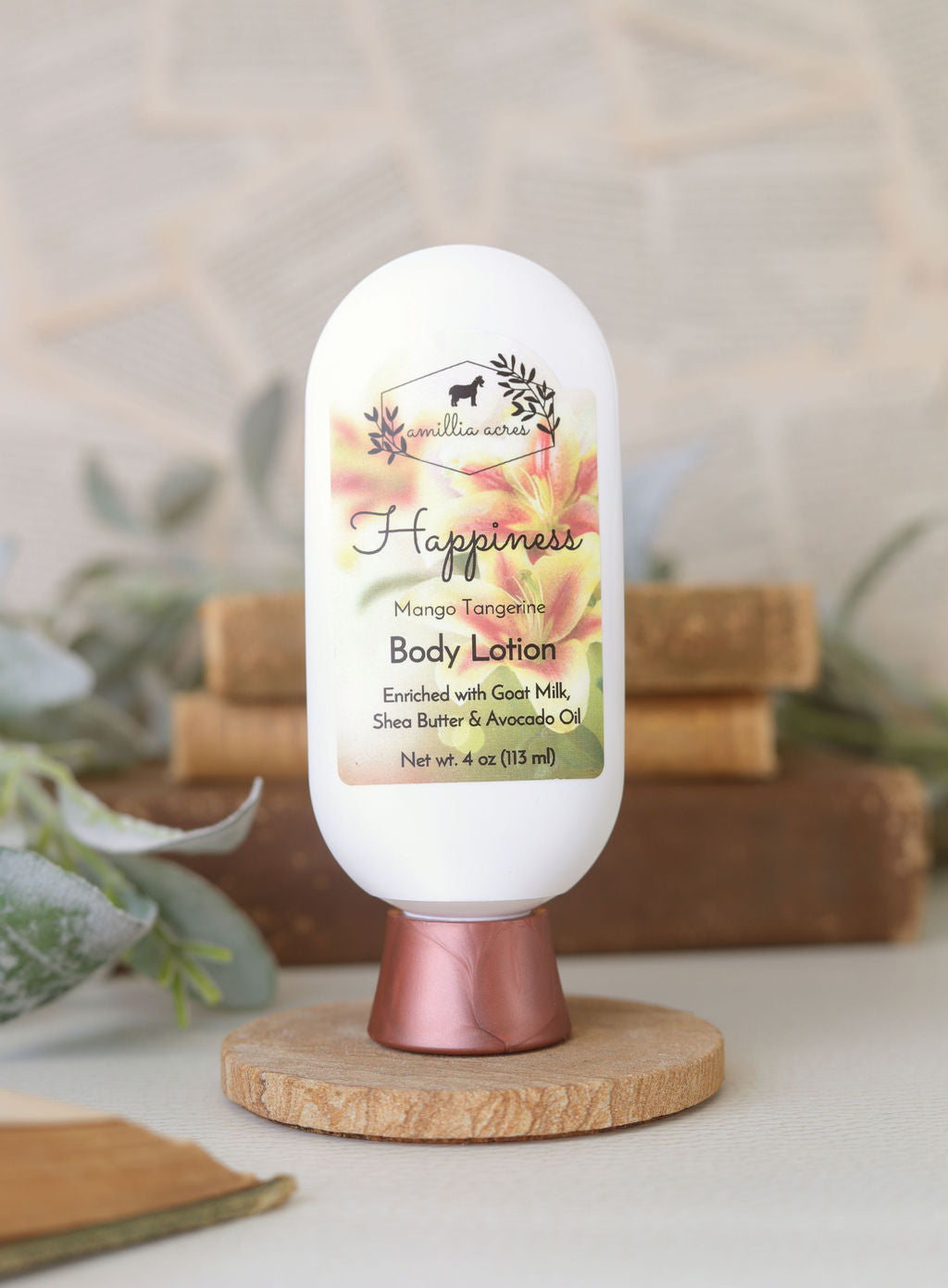 A bottle of Amillia Acres’ "Happiness" Goat Milk Lotion rests on a wooden stand, enriched with shea butter and avocado oil, surrounded by soft greenery with blurred books in the background.