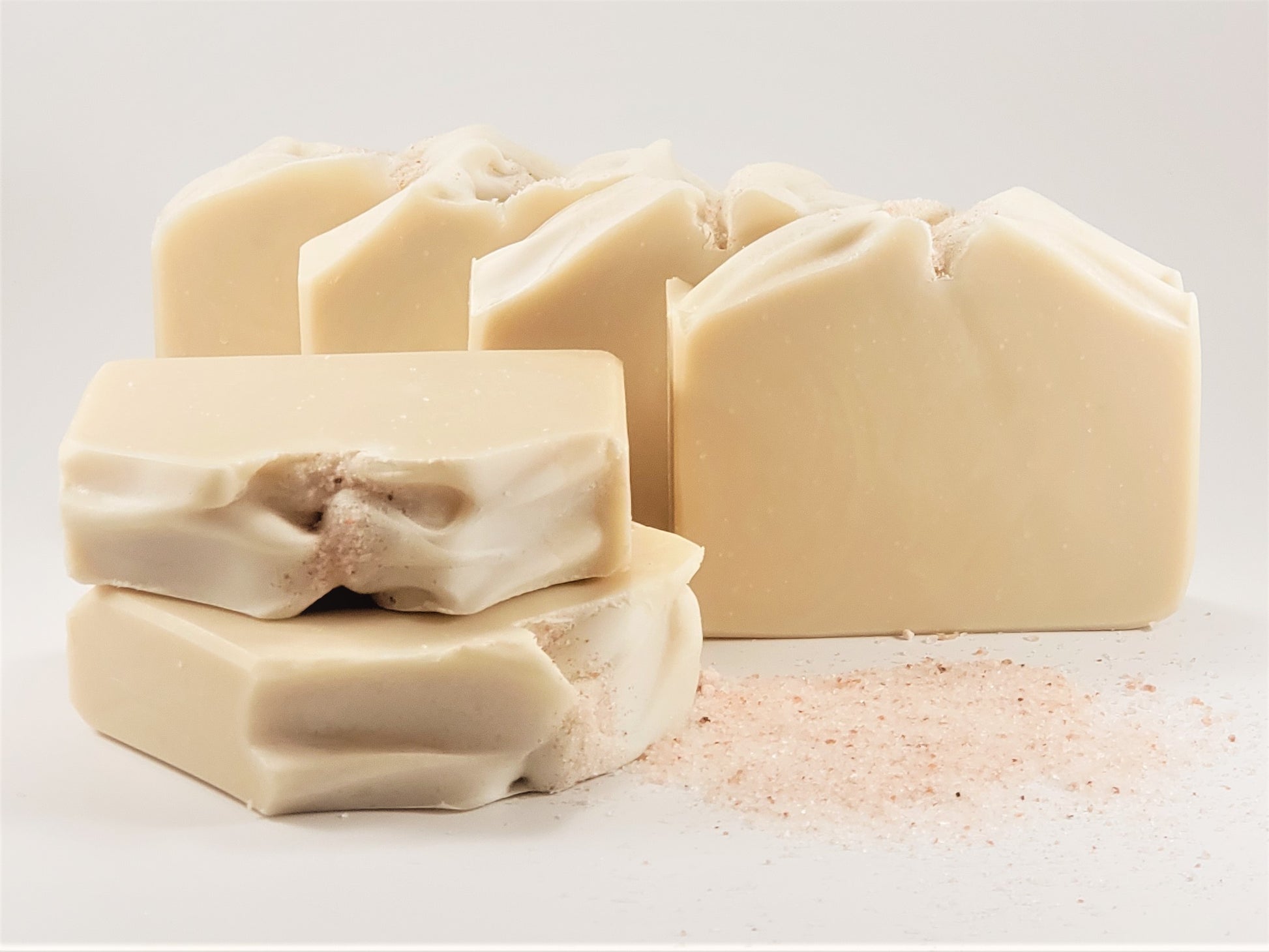 A stack of five bars of Simplicity Goat Milk Soap (Unscented) from Amillia Acres is arranged on a white surface. These soaps have a creamy hue with textured tops, and some pink salt scattered around them, offering an artisanal charm.