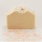 A bar of Simplicity | Goat Milk Soap by Amillia Acres with a textured top rests on a flat surface. Pink Himalayan salt specks contrast its creamy color, emphasizing its moisturizing properties against the plain white background.