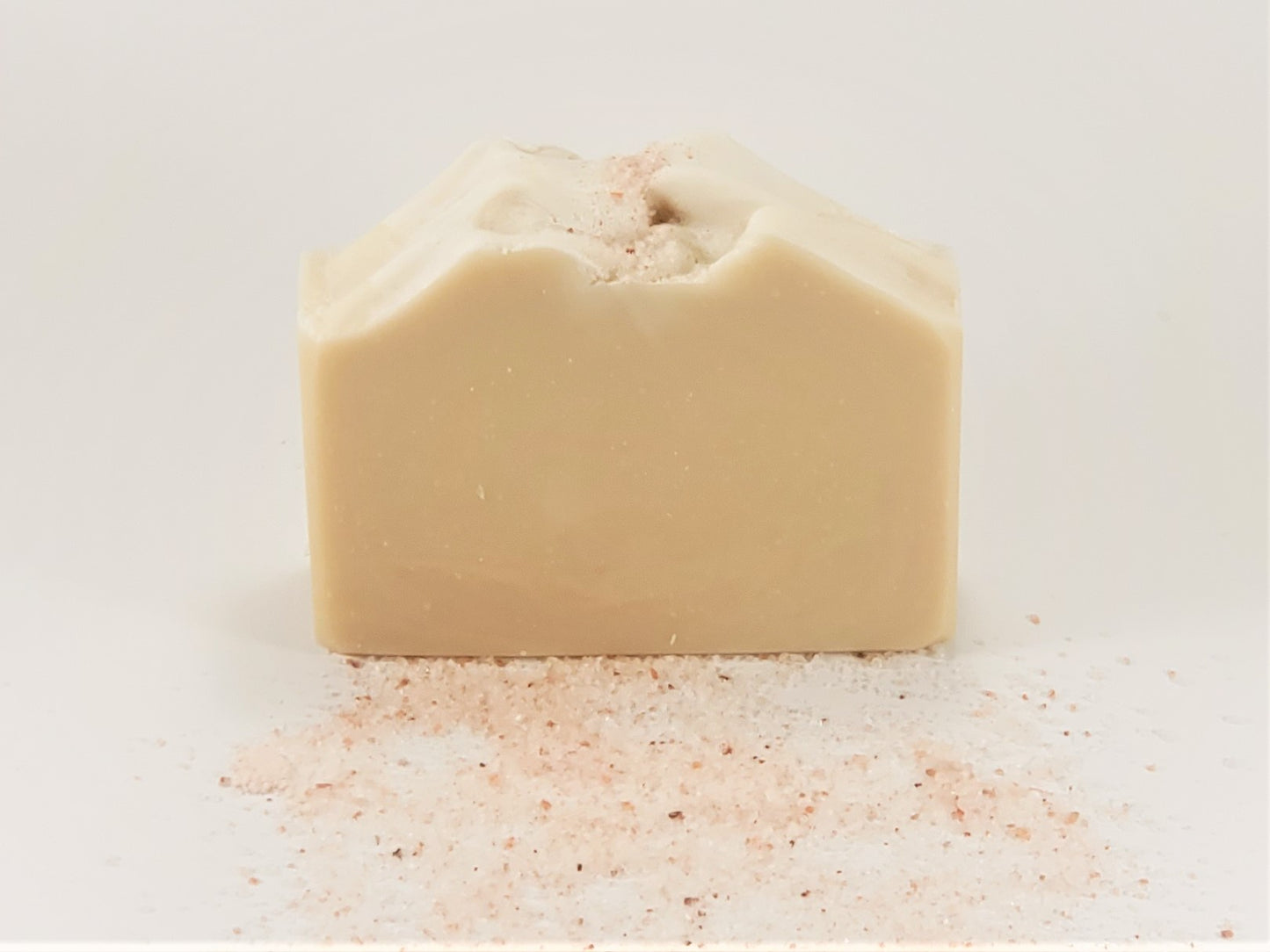 A rectangular bar of Amillia Acres Simplicity Goat Milk Soap (Unscented) with a textured top rests on a white background. Pink Himalayan salt is sprinkled on its surface and scattered around the base of this natural handmade soap.