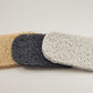 On a simple white background, three overlapping rectangular pads in beige, gray, and white showcase their textured, net-like surface. These Soap Savers from Amillia Acres are designed to extend the life of your soap.