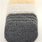 A stack of three Amillia Acres Soap Savers features a loofah-like texture; the top two have a pale color while the bottom one is dark gray. These are perfect for extending the life of your soap and maintaining cleanliness on any light background surface.