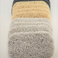 A stack of Soap Savers from Amillia Acres, crafted with curly, intertwined fibers in shades of gray, beige, and white, is elegantly arranged in a pile. These sophisticated soap savers help extend the lifespan of your soap by allowing it to dry between uses.