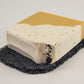 A handcrafted soap bar featuring a smooth beige top and a speckled white bottom rests elegantly on the Amillia Acres Soap Saver. This textured black dish is designed to extend the life of your soap, with its delicate particles enhancing both its functionality and aesthetic appeal.