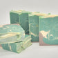 Five bars of Amillia Acres' "Relax" Goat Milk Soap, featuring natural oils and swirling designs in green, cream, and brown hues, are neatly stacked against a plain white background.