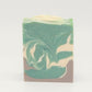 The Relax Goat Milk Soap by Amillia Acres features a marble-like swirl of green, cream, and brown with a subtle shimmer on top. Crafted from natural oils, it's set against a plain white background.