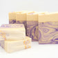 Five bars of Amillia Acres' Grace | Goat Milk Soap, adorned with purple and cream swirls, feature glitter specks and an elegant design. Some bars lie flat while others are upright, all set against a plain white background.